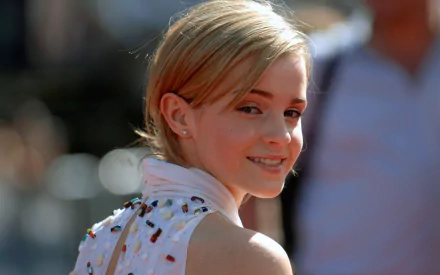 HD PC desktop wallpaper featuring a close-up of celebrity Emma Watson smiling over her shoulder with a blurred outdoor background.