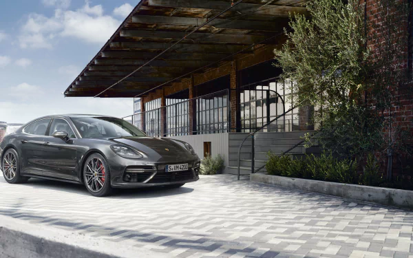 A sleek black Porsche Panamera parked beside a modern building, captured in a high-definition desktop wallpaper showcasing the luxury vehicle.