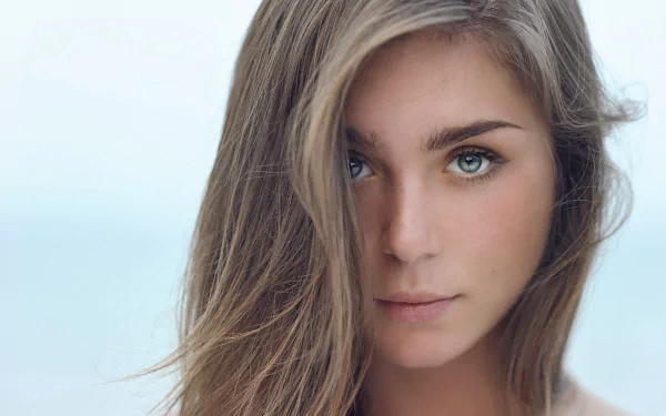 A close-up portrait of a model with hazel eyes and blonde hair, featuring a serene expression against a soft, blurred background. Ideal as a desktop wallpaper.