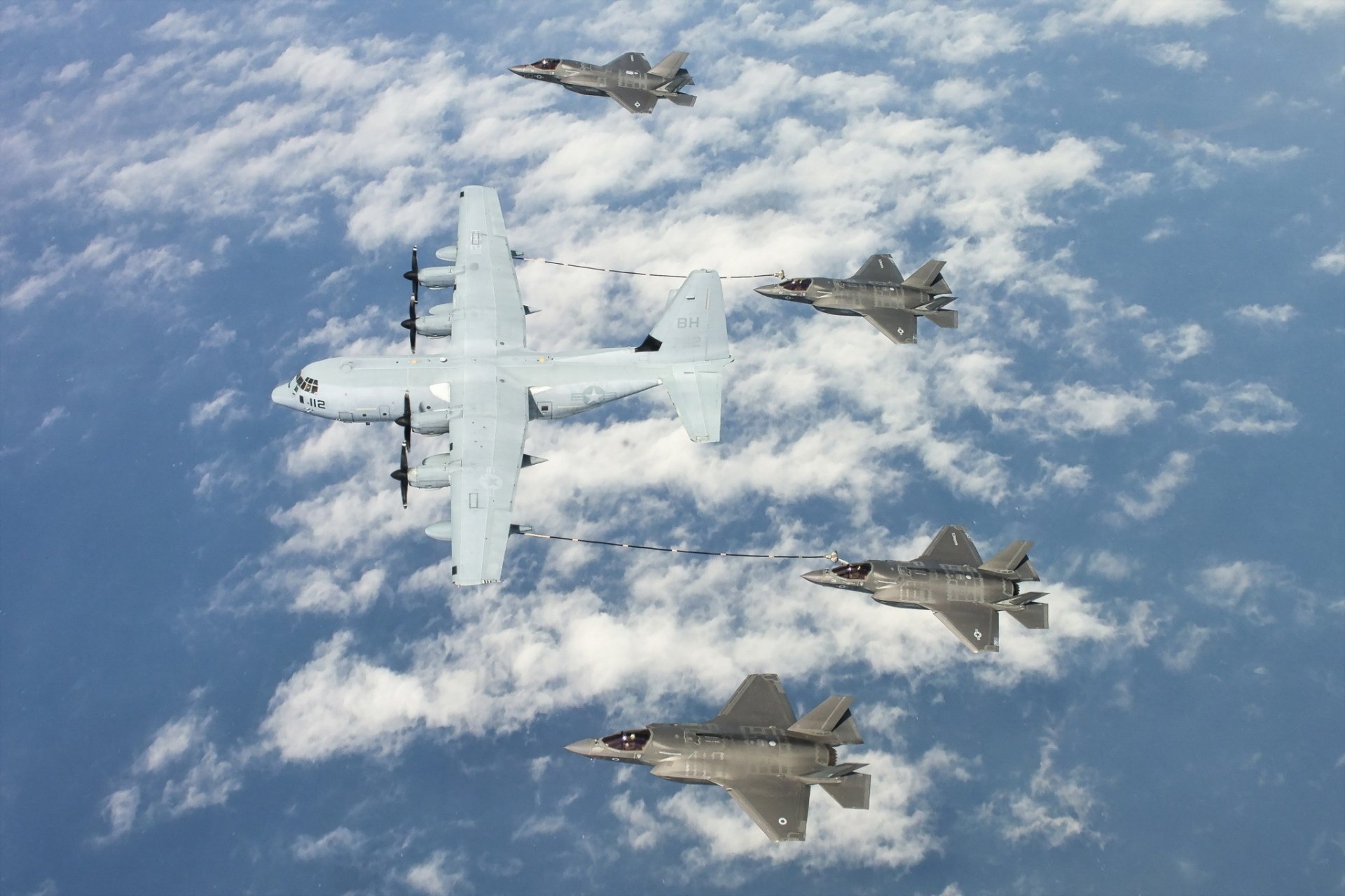 A Lockheed C-130 Hercules refuels four Lockheed Martin F-35 Lightning II warplanes mid-flight over clouds in this HD military aircraft wallpaper.