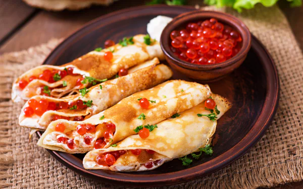Close-up of crepes filled with red caviar, garnished with herbs, displayed on a plate alongside a bowl of caviar, captured in 4K Ultra HD.