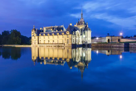 Château de Chantilly in France illuminated at dusk, its detailed architecture beautifully reflected on the calm water, captured in stunning 4K Ultra HD quality.