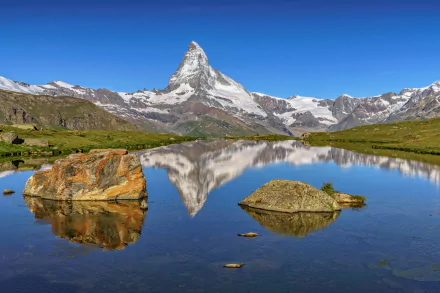 A stunning landscape of the Swiss Alps featuring the Matterhorn, reflected in a serene lake surrounded by lush greenery and rugged rock formations. A breathtaking natural scene.