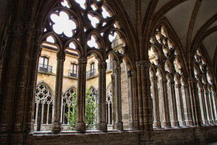 Gothic cloister of Oviedo Cathedral, Spain, sunlit pointed arches overlooking the inner courtyard — 4K Ultra HD PC desktop wallpaper background.