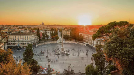 Sunset over Rome’s cityscape featuring an obelisk at the center of a bustling square, with historic buildings and trees framing the vibrant urban scene.