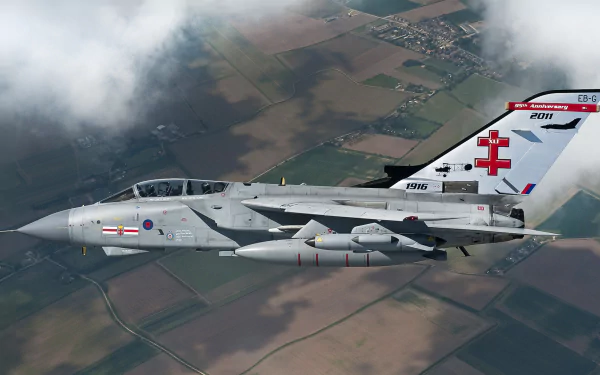 A Panavia Tornado jet fighter soars through a cloudy sky, showcasing its military prowess over a patchwork of fields below. High-definition desktop wallpaper capturing aerial strength.