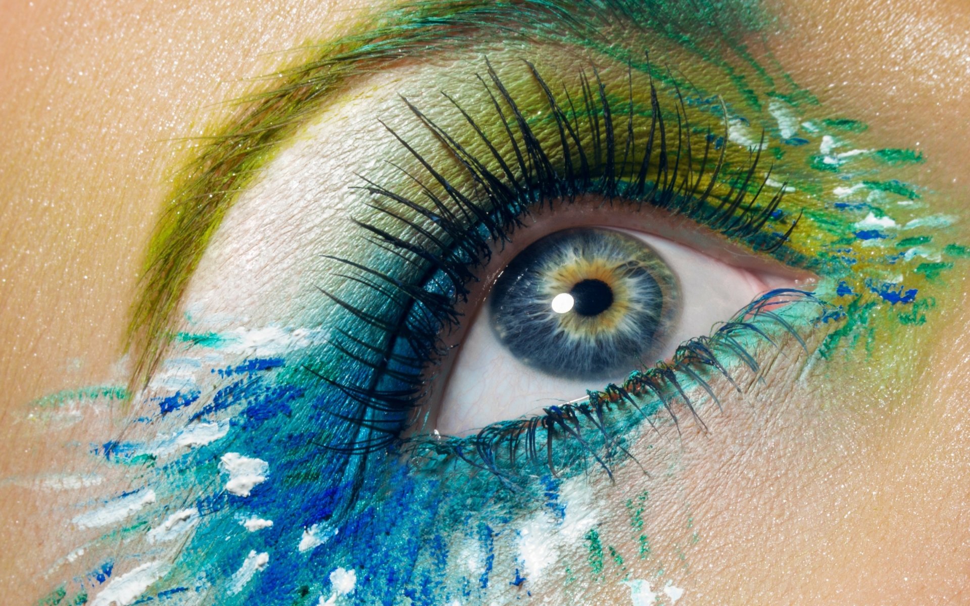 Close-up of a woman's eye with vivid blue, green and yellow makeup splashes, dramatic lashes and textured pigment — 2K Quad HD PC desktop wallpaper/background.