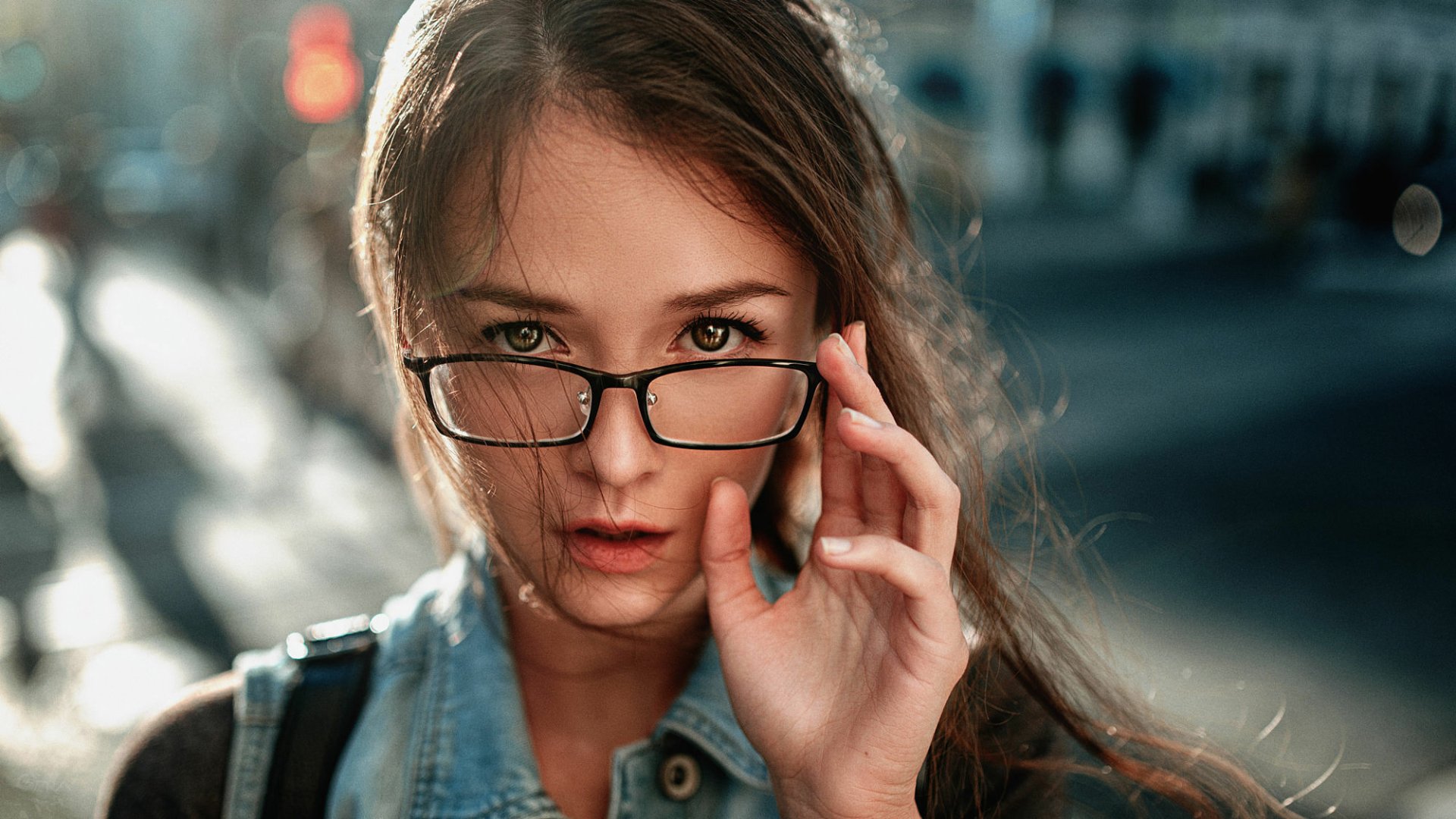 A close-up of a brunette woman with brown eyes wearing glasses, looking confidently at the camera. The image features soft lighting, creating a striking HD desktop wallpaper.