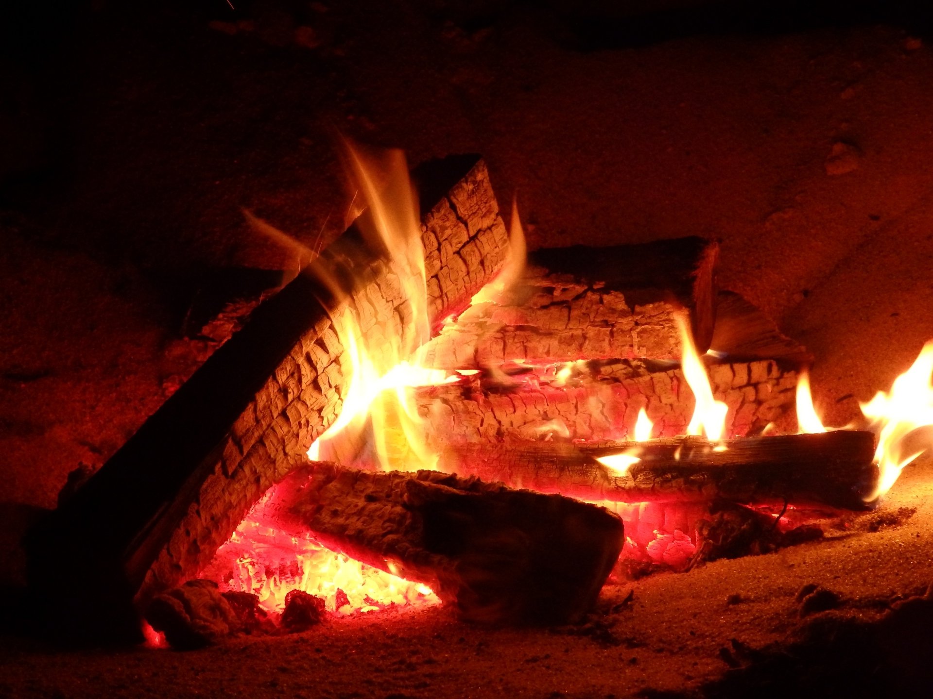 HD desktop wallpaper showcasing a close-up photograph of a campfire with glowing wood and vibrant flames.