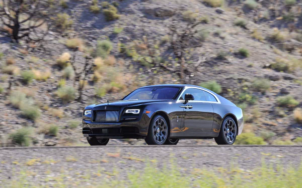 Black Rolls-Royce Wraith driving on a desert road, captured in sharp 4K UHD detail as a sleek luxury vehicle against a rugged natural backdrop.