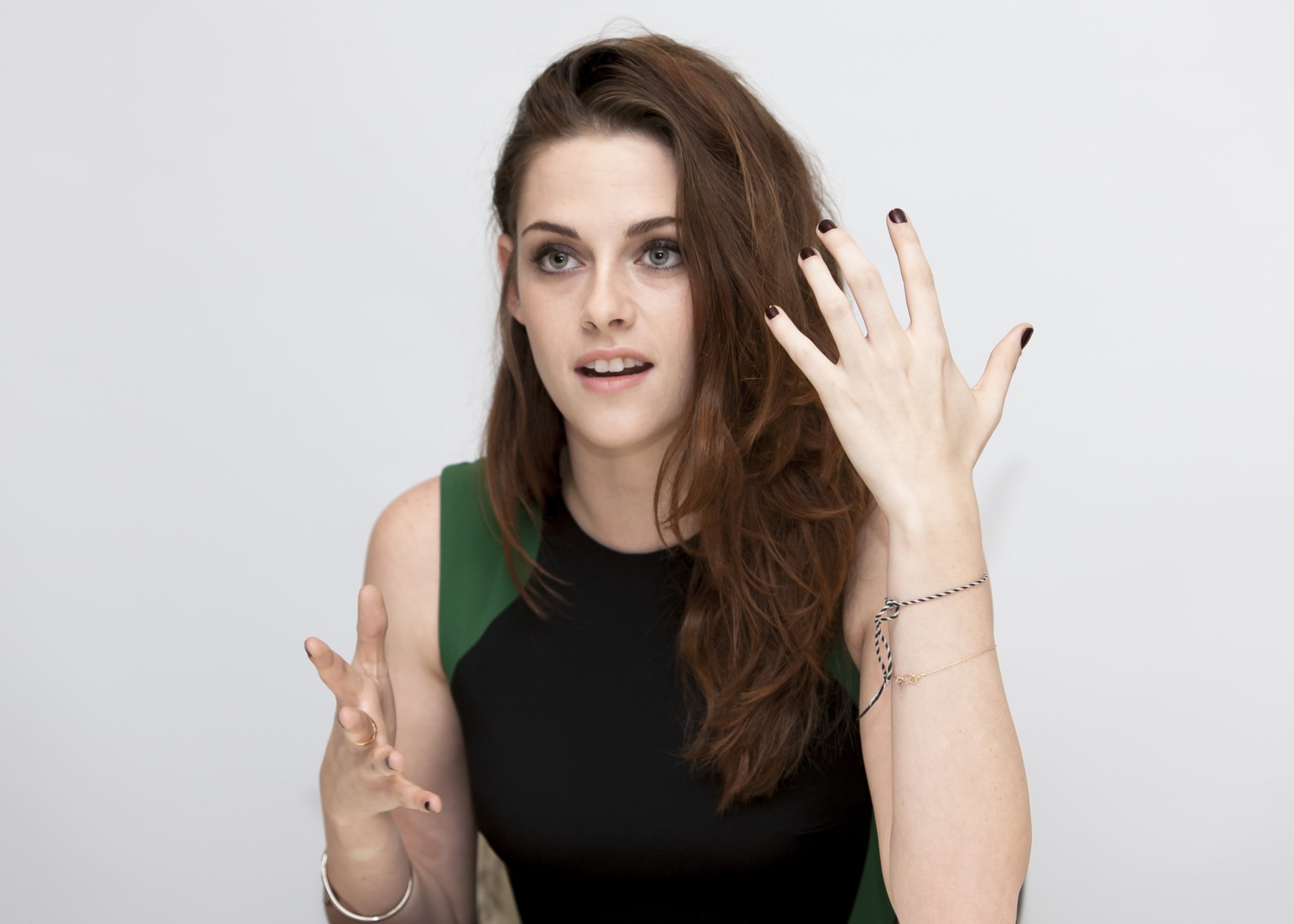 A close-up of Kristen Stewart, displaying expressive hand gestures while wearing a black and green outfit. The image serves as a stunning 4K Ultra HD desktop wallpaper.