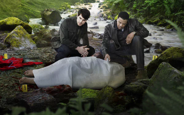 Two detectives investigate a crime scene by a stream, examining a body covered with a white sheet, set in a lush, green environment. This HD wallpaper features scenes from the TV show Grimm.