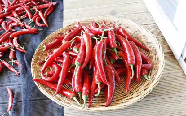 Bright red chili peppers arranged in a woven basket and scattered on a cloth, captured in a crisp 4K Ultra HD PC desktop wallpaper and background.