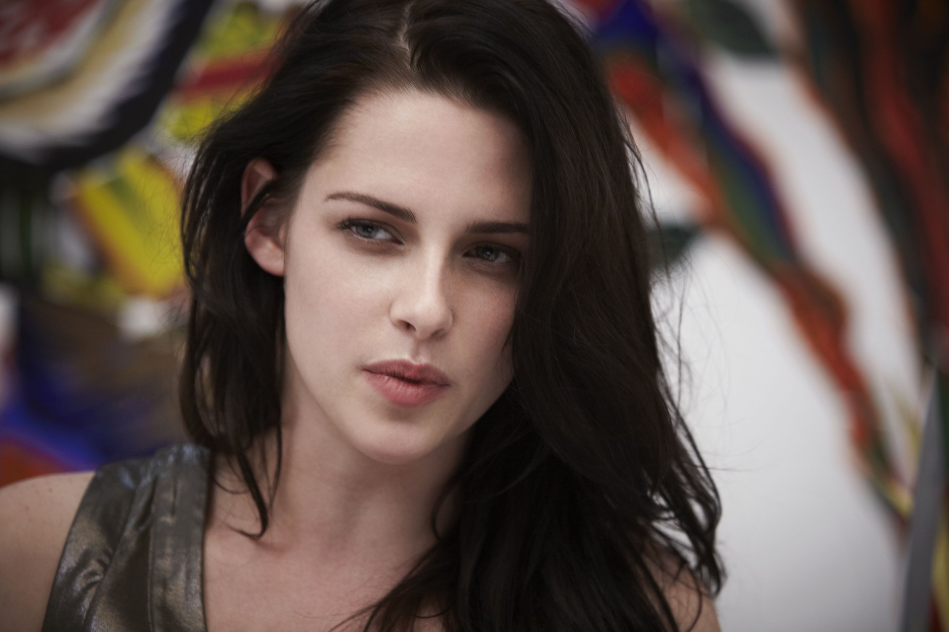 A close-up image of Kristen Stewart, showcasing her expressive gaze, set against a vibrant abstract background, designed for a 4K Ultra HD PC desktop wallpaper.