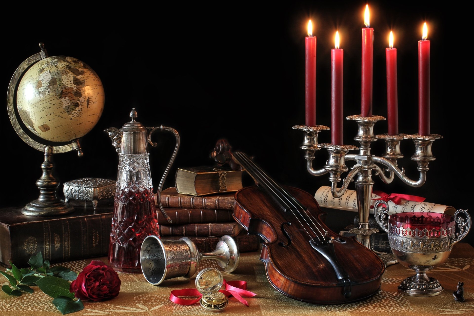 HD desktop wallpaper featuring a still life composition with a globe, violin, lit red candles in a silver candelabra, vintage books, and antique glassware on a dark background.