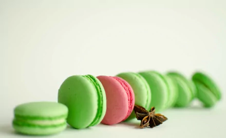 HD desktop wallpaper featuring a row of green and one pink macaron sweets arranged with star anise on a clean white background.