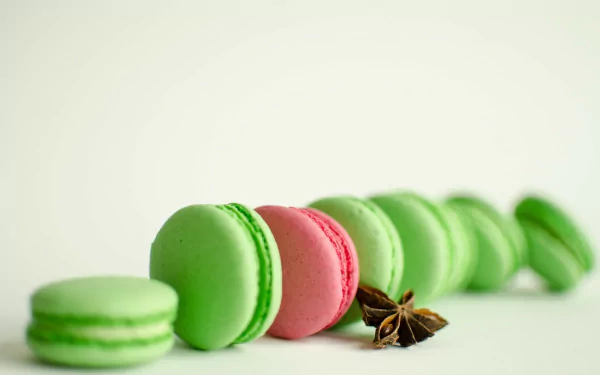 HD desktop wallpaper featuring a row of green and one pink macaron sweets arranged with star anise on a clean white background.
