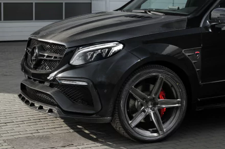 Close-up of a sleek black Mercedes-Benz GL-Class SUV parked on a paved surface, showcasing its front grille, headlight, and large alloy wheel with red brake calipers.