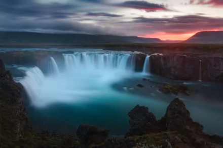 HD desktop wallpaper of Iceland’s Goðafoss waterfall cascading under a dramatic sky at sunset, showcasing stunning natural beauty and rugged landscape.