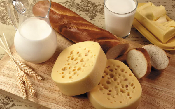 A still life featuring butter, bread, cheese, and milk, arranged on a wooden board, showcases the simplicity and richness of delicious food in vibrant 4K Ultra HD clarity.