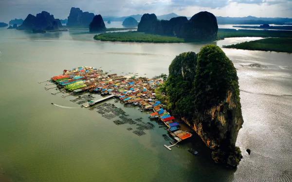 Aerial view of a vibrant man-made village on an island in Phuket, Thailand, surrounded by lush mountains and calm waters, showcasing the region's unique beauty.