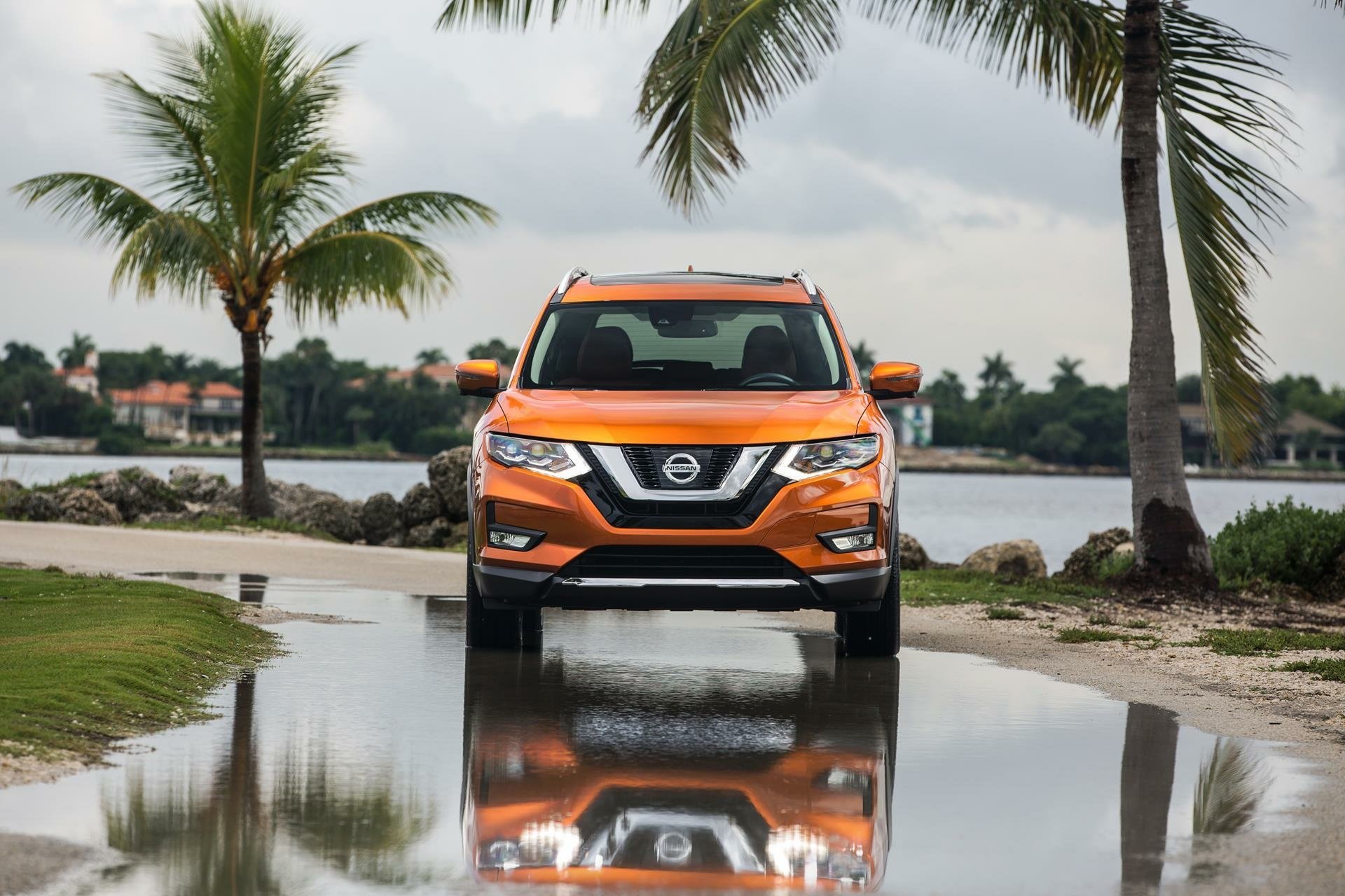 HD desktop wallpaper featuring an orange Nissan Rogue SUV parked on a reflective wet surface with palm trees and water in the background.