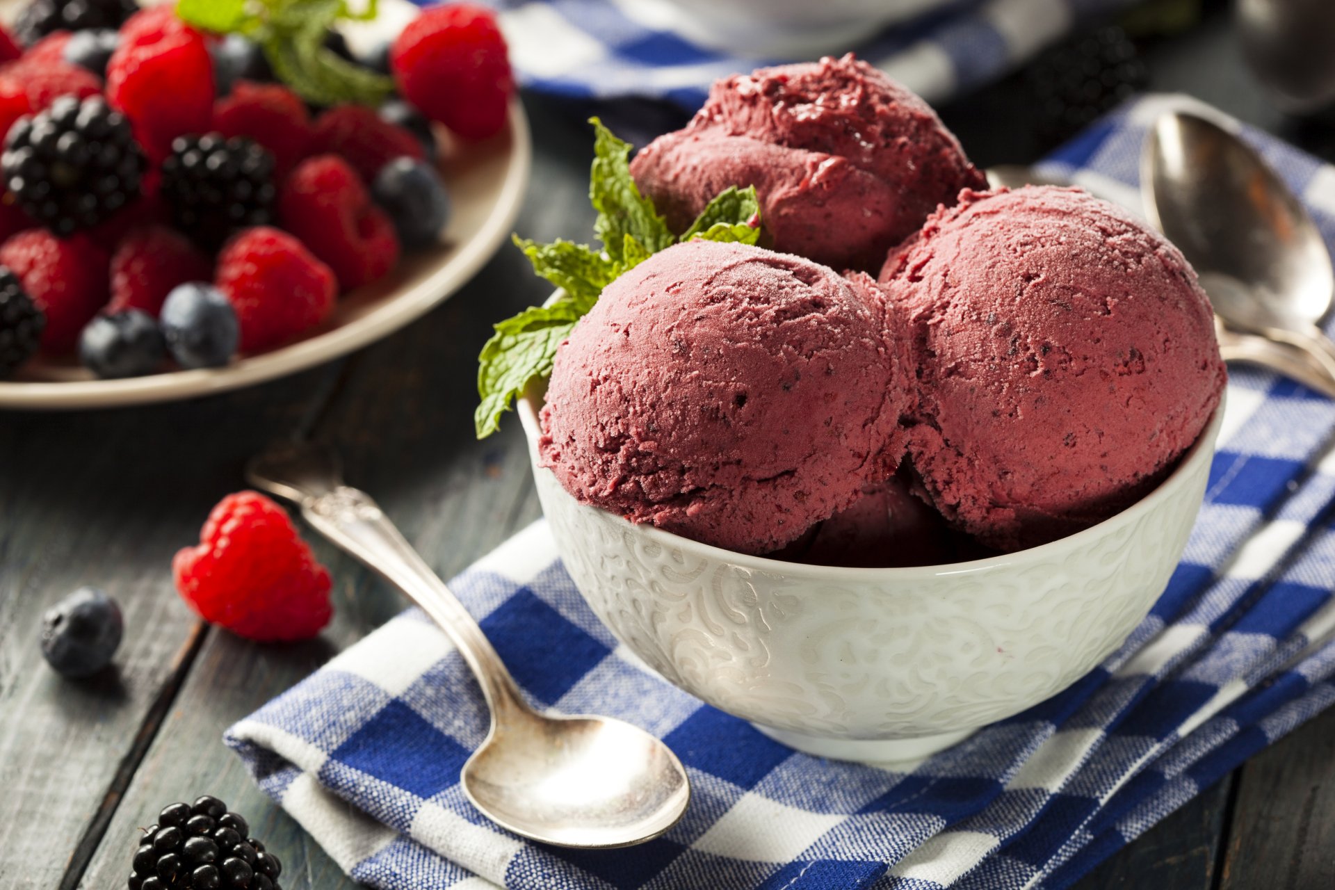 A bowl of mixed berry ice cream with blueberry, blackberry, and raspberry, set on a checkered cloth with fresh berries in the background, captured in 4K Ultra HD.