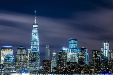 Nighttime view of New York City's skyline featuring the illuminated One World Trade Center and surrounding skyscrapers, captured as a high-definition desktop wallpaper.