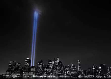 Selective color image of New York City skyline at night with two bright light beams shining upward from skyscrapers, highlighting the man-made urban landscape.