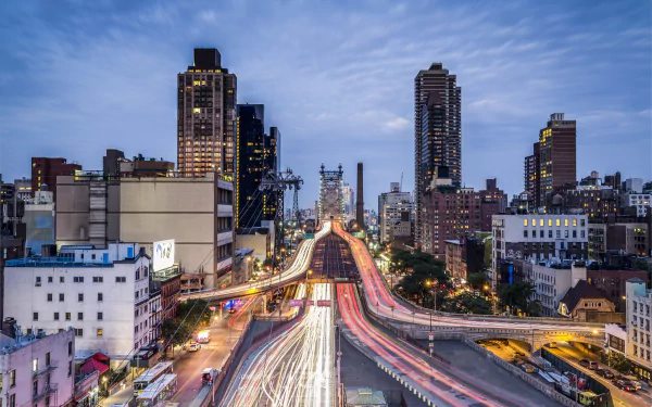 Nighttime long-exposure view of Manhattan and the Queensboro Bridge with streaking road light trails and skyline buildings, an HD PC desktop wallpaper of New York City, USA.