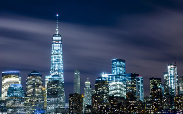 Nighttime view of New York City's skyline featuring the illuminated One World Trade Center and surrounding skyscrapers, captured as a high-definition desktop wallpaper.