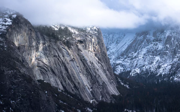 5K Ultra HD PC desktop wallpaper: winter mountain landscape with a sheer cliff face, snow-covered peaks, misty clouds and dark forested valley.