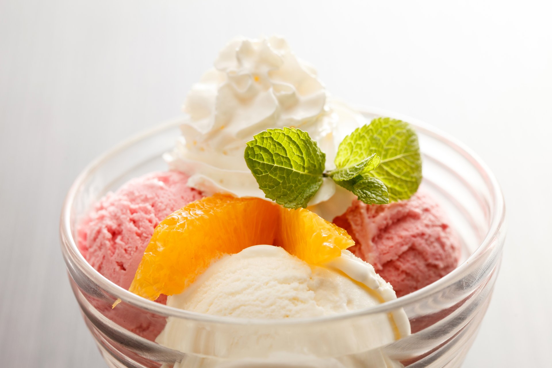A vibrant 4K Ultra HD desktop wallpaper featuring a glass bowl of strawberry and vanilla ice cream, topped with whipped cream, orange slices, and fresh mint leaves.