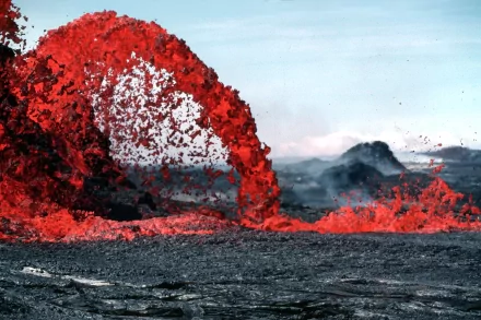 HD desktop wallpaper featuring vibrant red lava flowing from a volcano amidst a rugged landscape, against a backdrop of a clear sky and distant mountains.