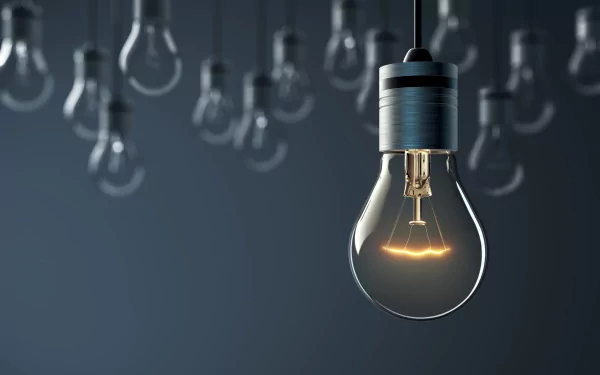 Glowing incandescent bulb in sharp focus with blurred hanging bulbs behind — 2K Quad HD PC desktop wallpaper of man-made lighting