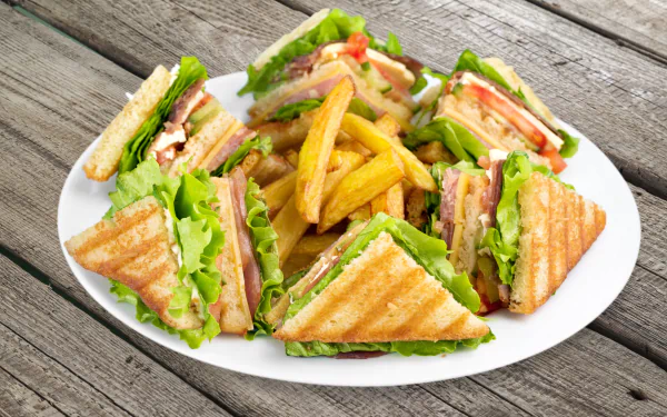 4K Ultra HD desktop wallpaper featuring a plate of sandwiches with lettuce and tomato, accompanied by golden French fries on a rustic wooden table.