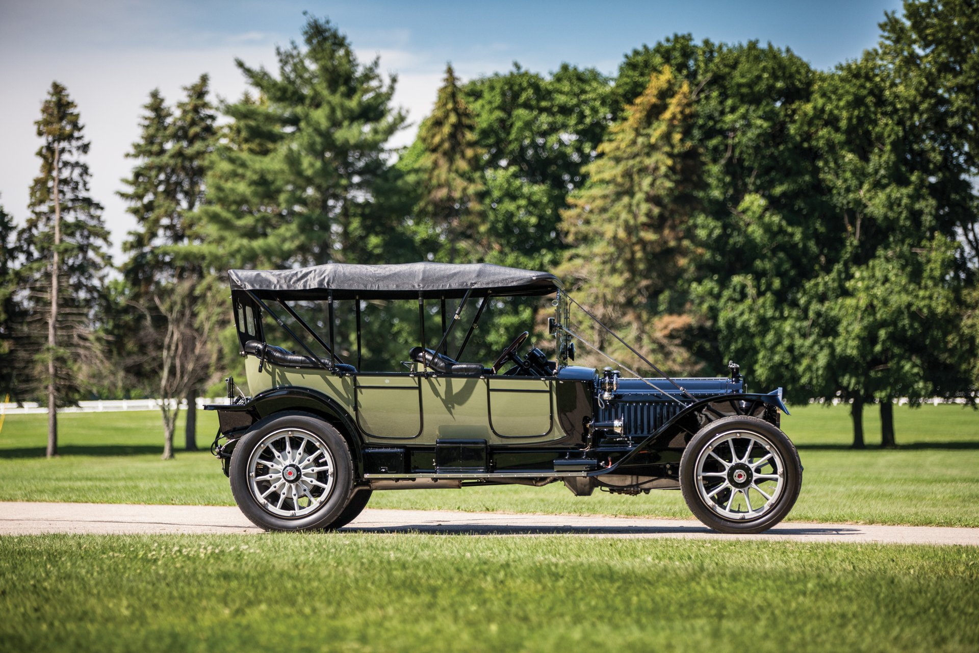 Vintage 1914 Packard Six 5-passenger Touring car parked on a grassy path with lush green trees in the background, captured in high definition for PC desktop wallpaper.