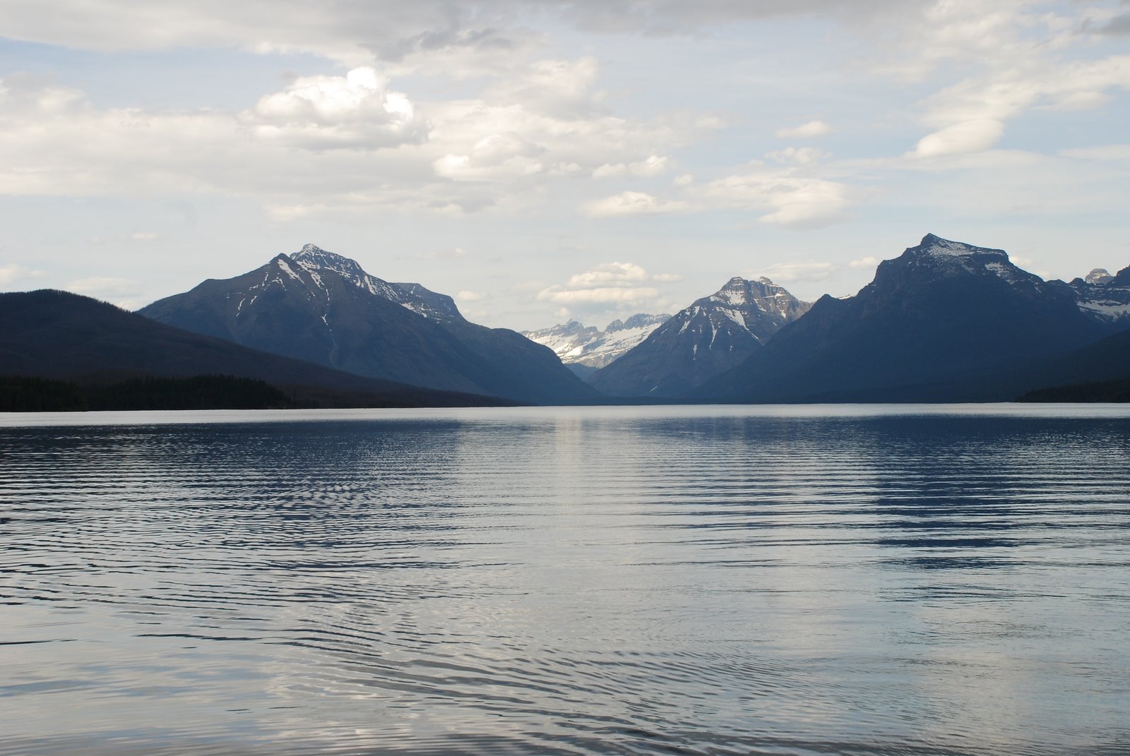 HD desktop wallpaper featuring a serene nature landscape with calm water and distant snow-capped mountains under a partly cloudy sky.