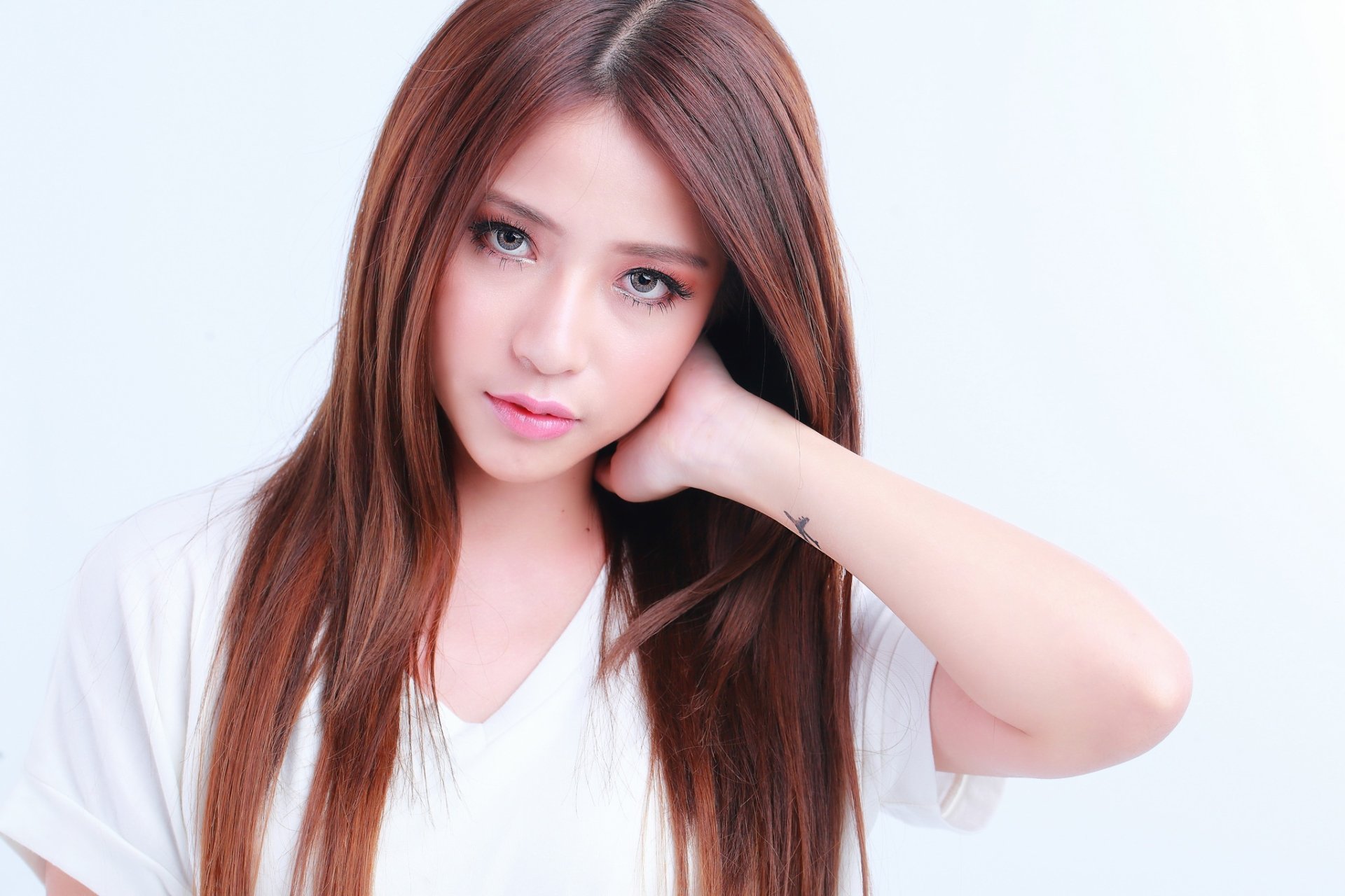 HD desktop wallpaper featuring an Asian woman with long brunette hair, modeling a casual white top with her hand resting on her neck, set against a plain background.