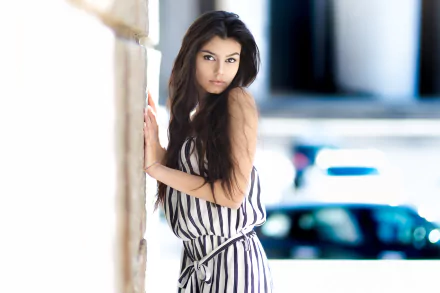 HD desktop wallpaper featuring a brunette woman with brown eyes in a striped outfit, leaning against a stone wall with a blurred background.