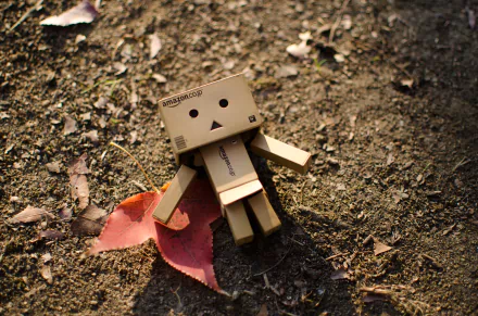 Danbo figure lying on earthy ground with scattered leaves in 4K Ultra HD detail, designed as a captivating PC desktop wallpaper in the Misc category.