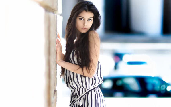 HD desktop wallpaper featuring a brunette woman with brown eyes in a striped outfit, leaning against a stone wall with a blurred background.