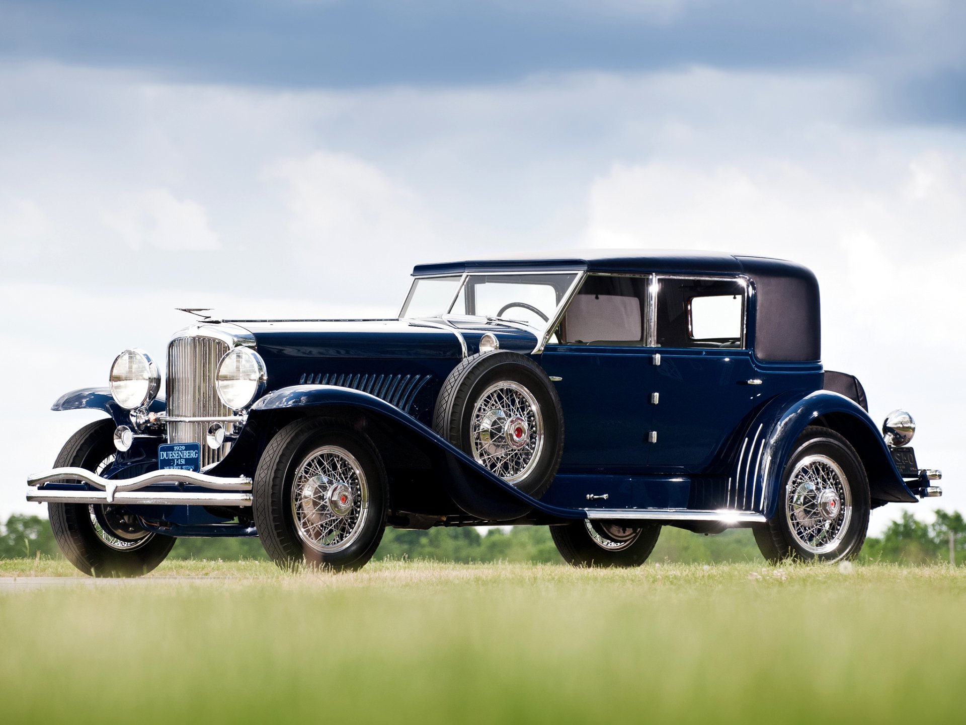 A vintage 1929 Duesenberg Model J Sport Sedan in dark blue, showcased as an HD PC desktop wallpaper and background.
