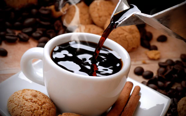 Steaming black coffee being poured into a white cup surrounded by cinnamon sticks, biscuits, and scattered coffee beans on a warm-toned HD desktop wallpaper.