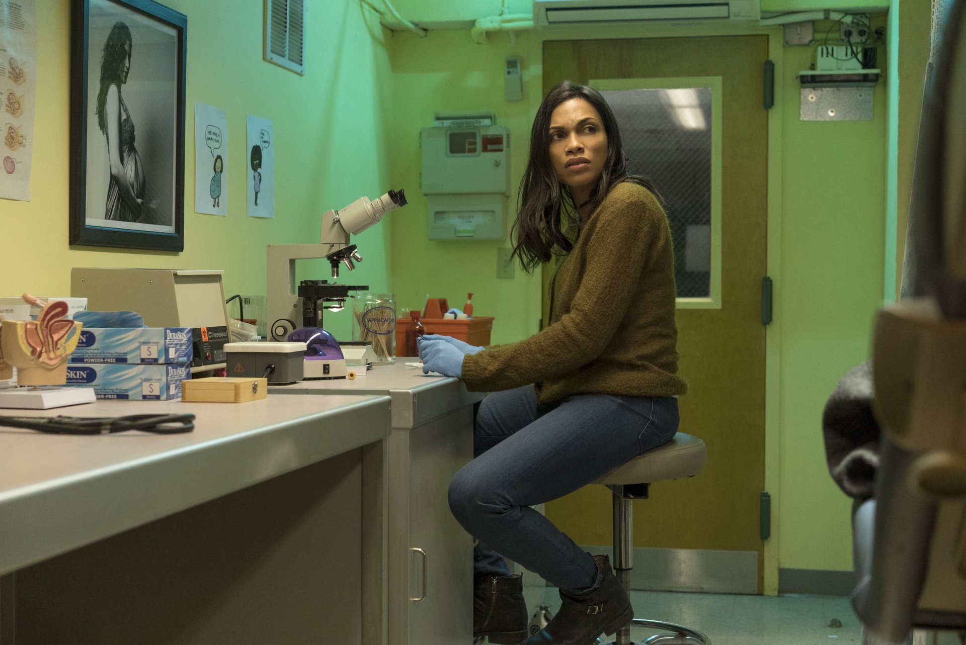 HD PC desktop wallpaper from the TV show Luke Cage featuring a woman sitting on a stool in a green-lit room with medical and office supplies.