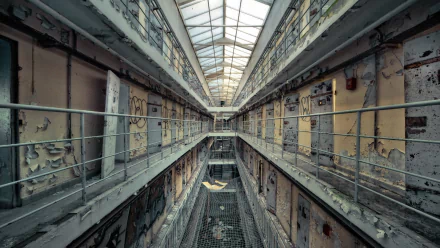 An eerie, abandoned prison interior featuring peeling walls and empty cells, with sunlight filtering through a skylight, creating a haunting atmosphere.