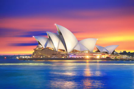 A stunning sunset over Sydney Harbour, featuring the iconic Sydney Opera House, reflects vibrant colors in the water, creating a beautiful scene emblematic of Australia's charm.