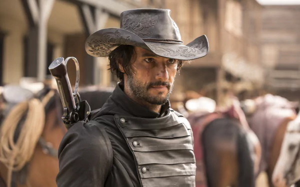 A close-up of Hector Escaton, played by Rodrigo Santoro, in cowboy attire from the TV show Westworld, featuring a rugged look and a dramatic backdrop of horses and a western setting.