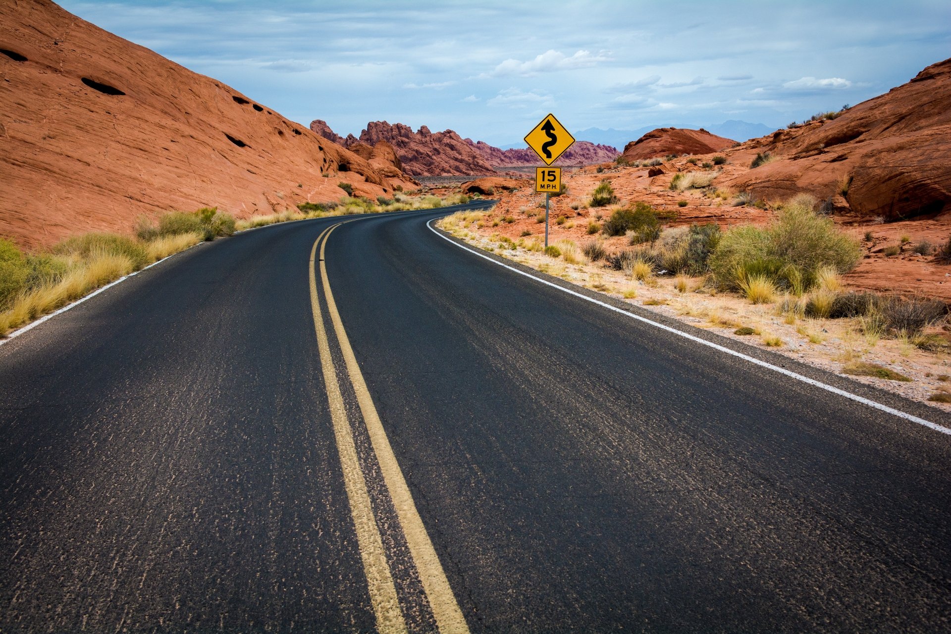 4K Ultra HD wallpaper featuring a winding man-made road through a desert landscape with red rock formations under a partly cloudy sky.