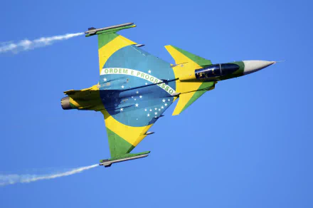 A Saab JAS 39 Gripen jet fighter adorned with the Brazilian flag flies through a clear blue sky, showcasing its military prowess and vibrant colors in a striking HD wallpaper.
